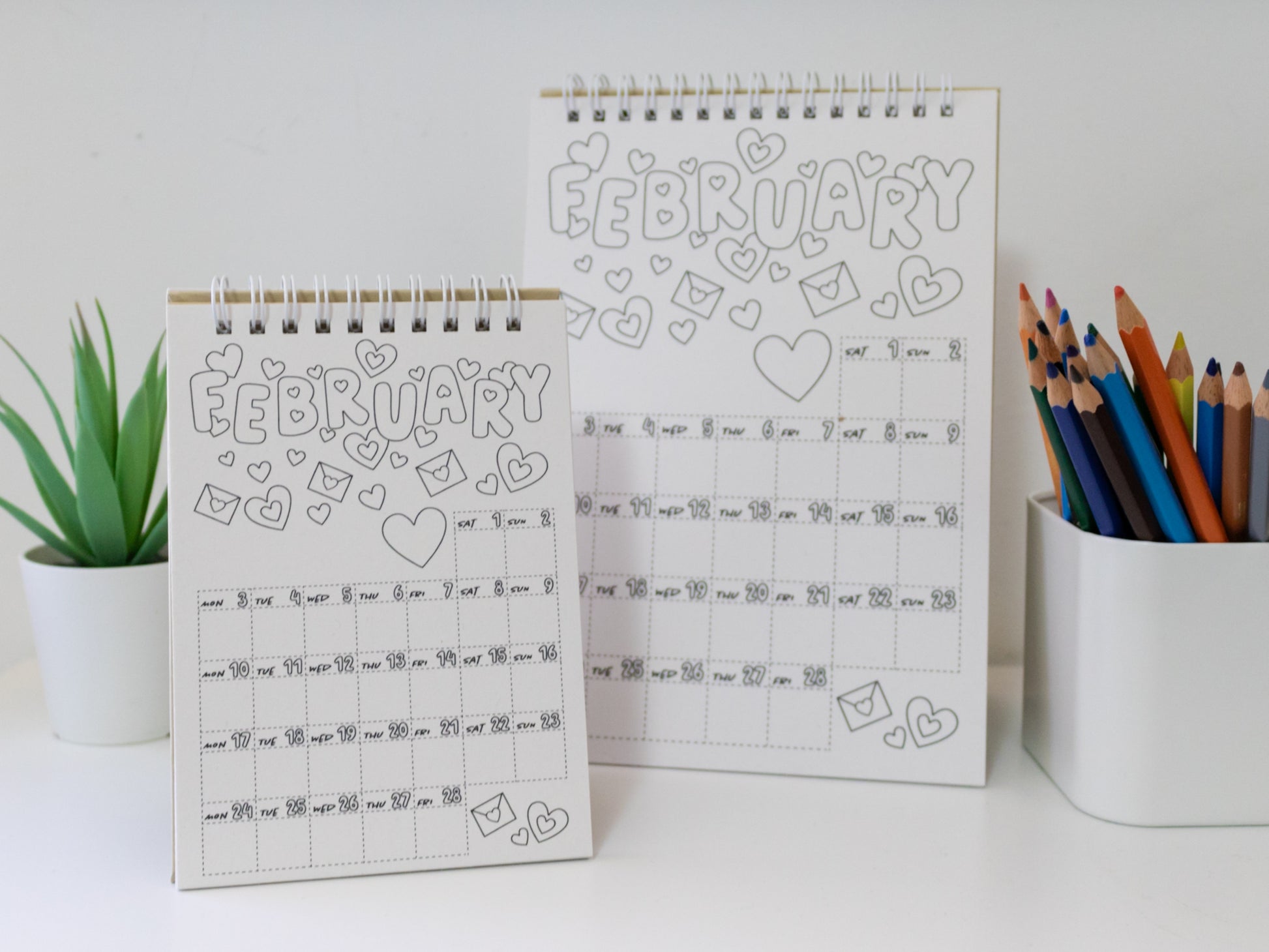 Two 2026 colouring desk calendar design on a white surface with coloured pencils - February pages