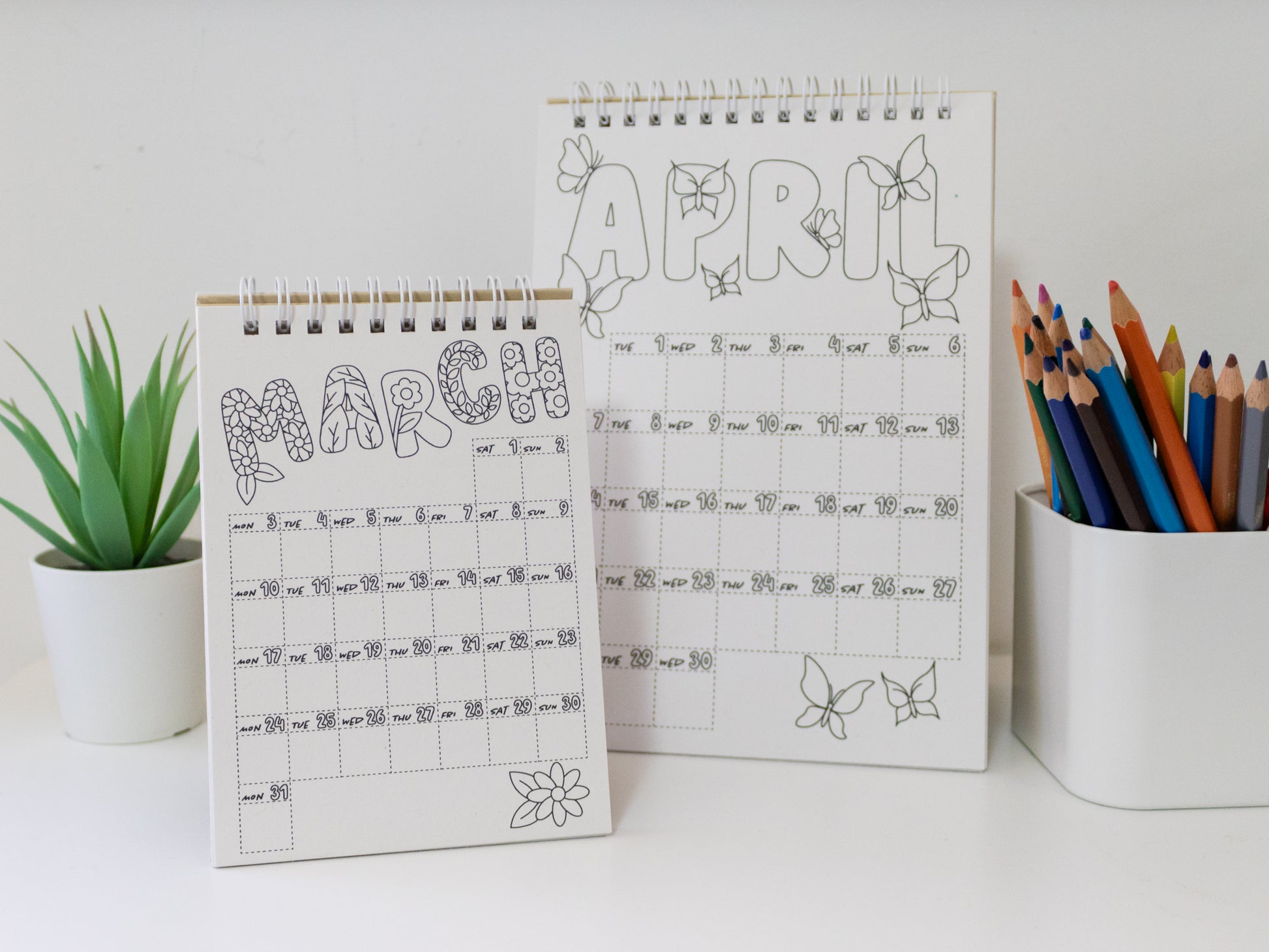 Two 2026 colouring desk calendars on a white surface with coloured pencils - April & March pages