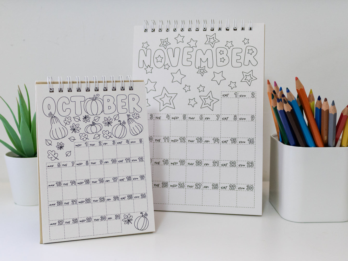 Two 2026 colouring desk calendars on a white surface with coloured pencils - October & November pages
