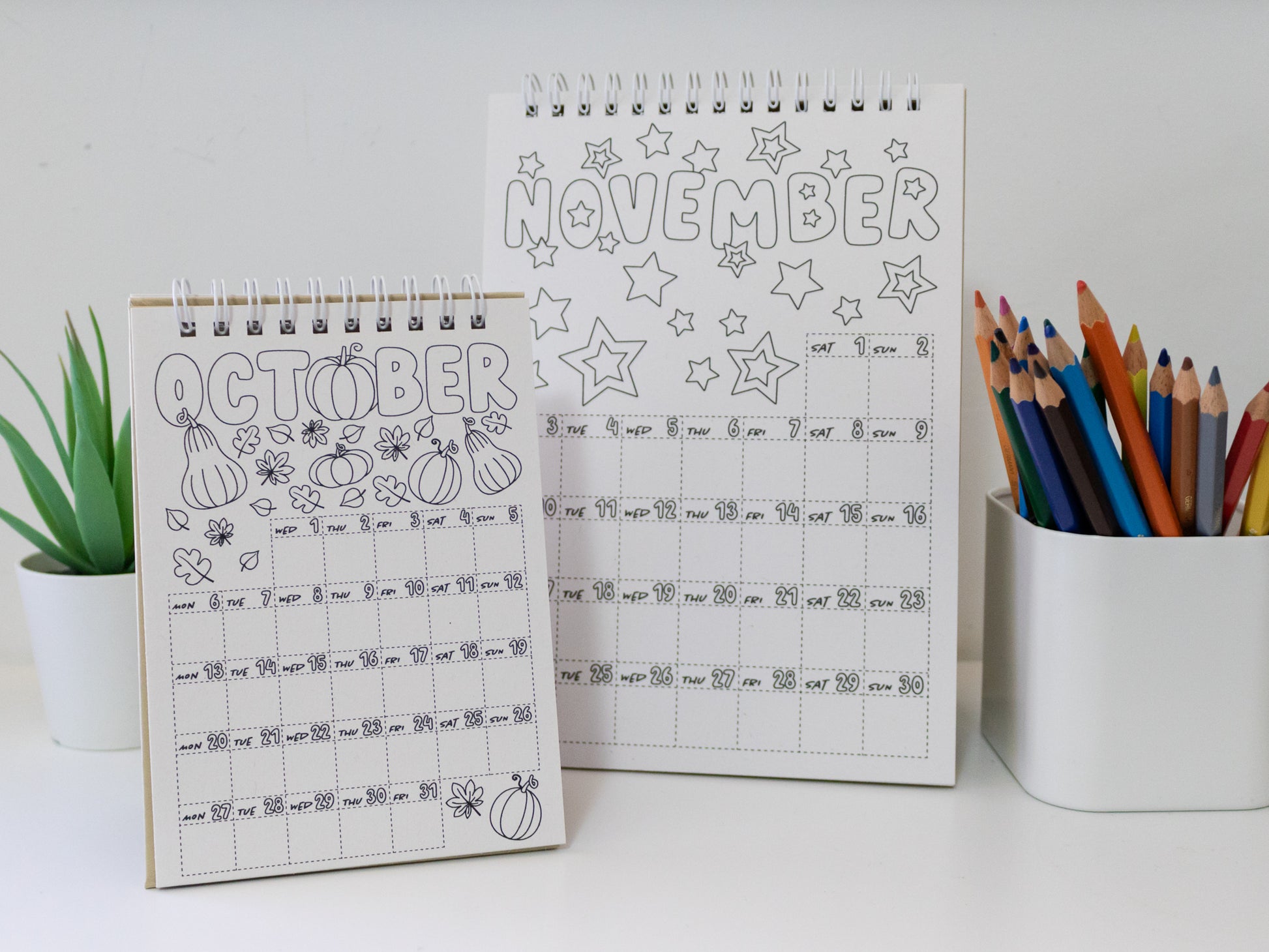 Two 2026 colouring desk calendars on a white surface with coloured pencils - October & November pages