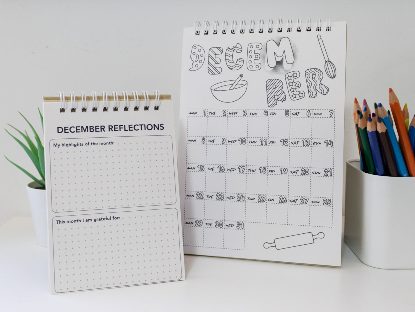 Two 2026 colouring desk calendars on a white surface with coloured pencils - December pages front and back