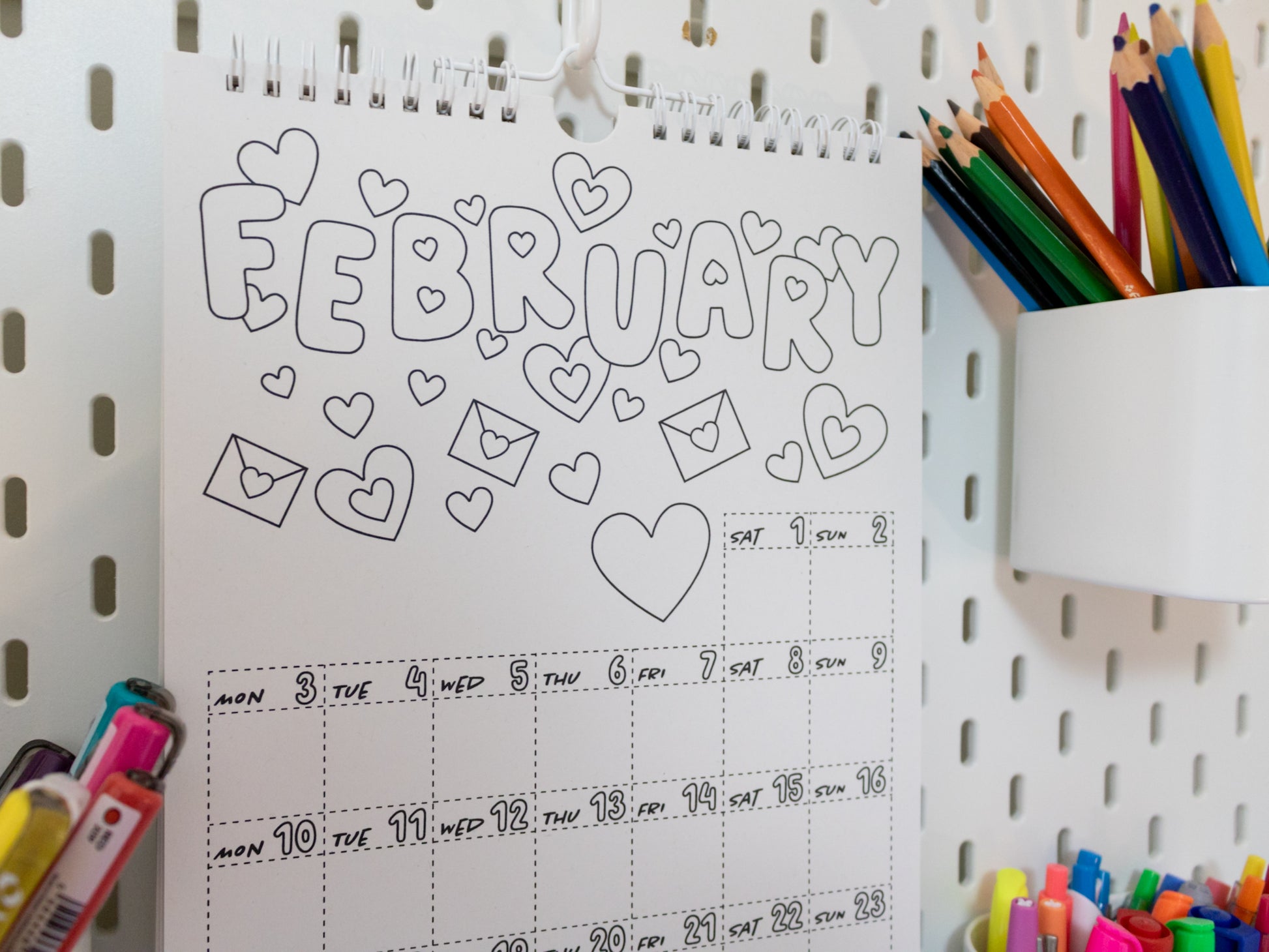 2026 Colouring Calendar on a pegboard with markers and crayons - February page