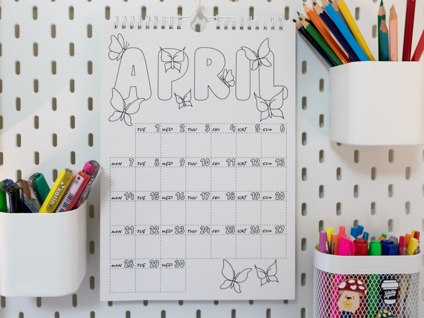2026 Colouring Calendar on a pegboard with markers and crayons - April page