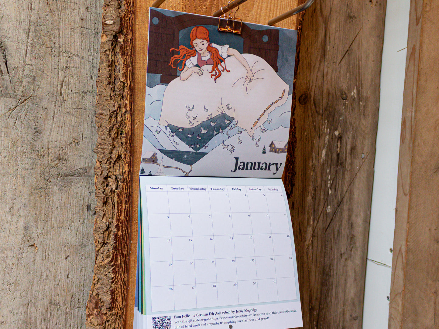 Calendar with January page showing a illustration of a woman with red hair, hanging on a wooden surface.