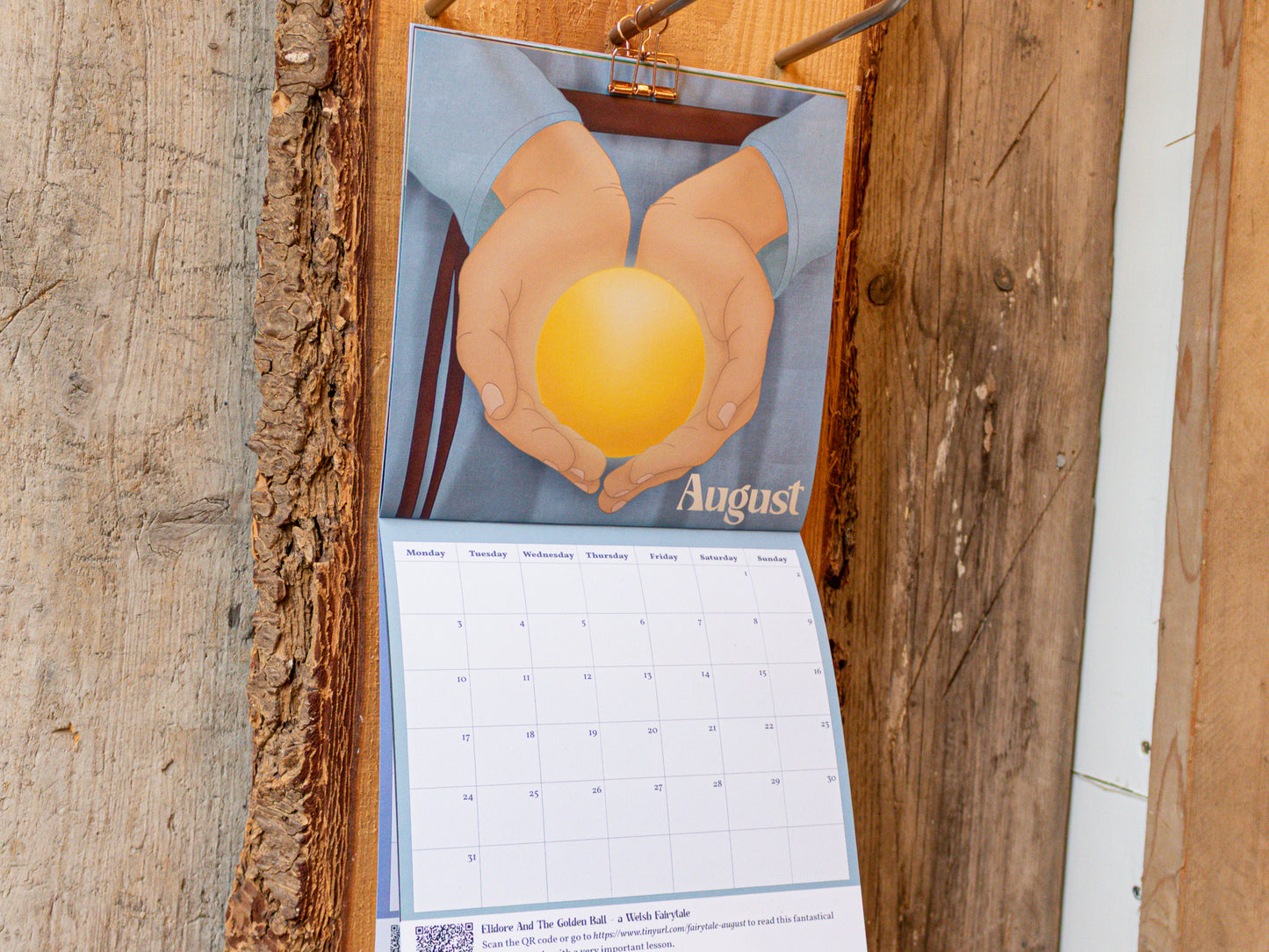 2026 Fairytale Calendar with hands holding a golden ball illustration on a wooden surface