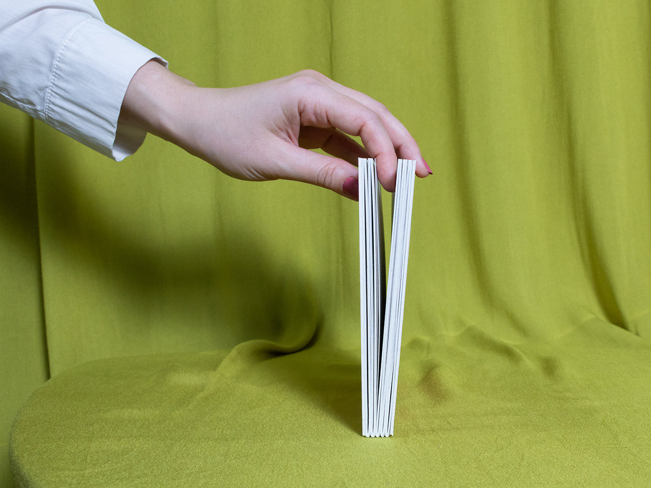 Hand holding a sketchbook against a green fabric background