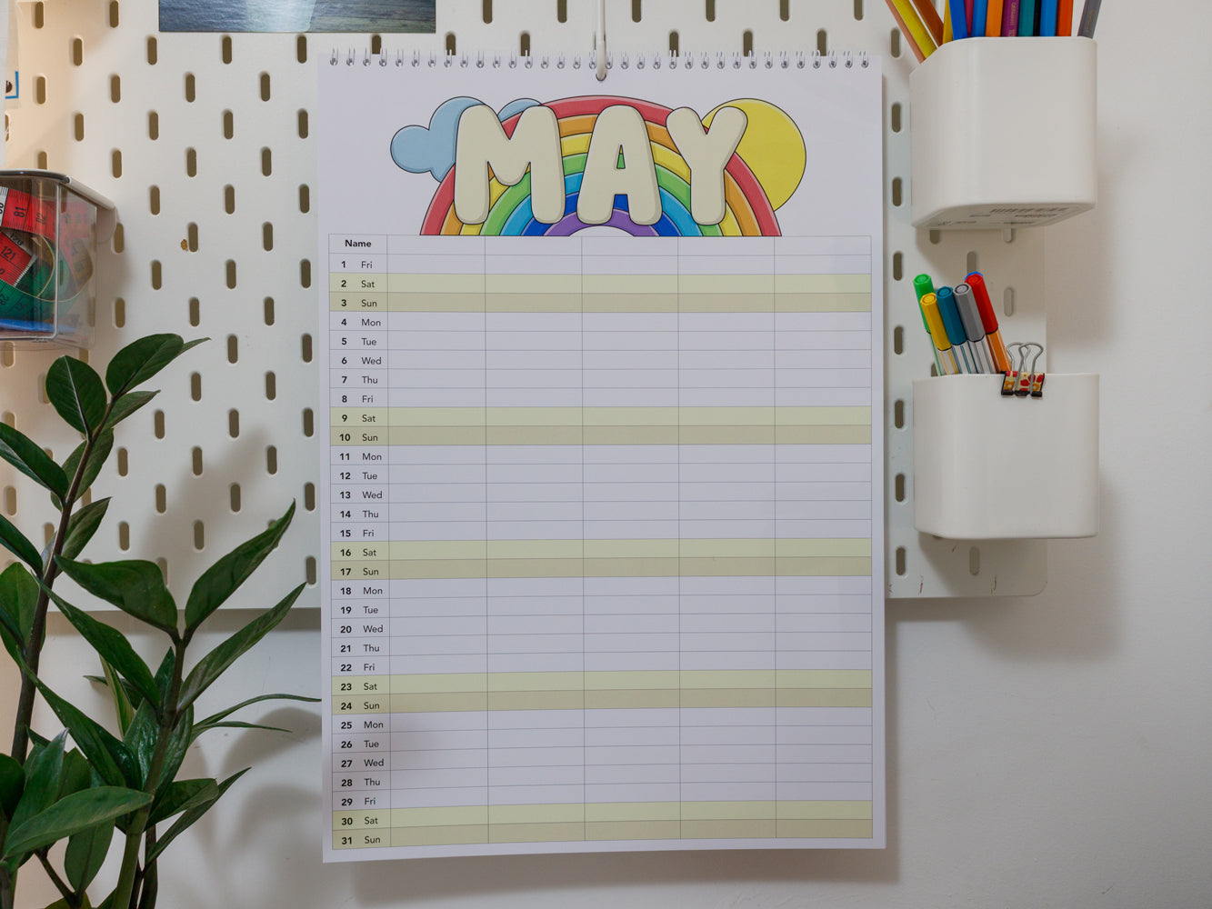 2026 A3 Family Planner: May page with rainbow design on a white wall with stationery items.