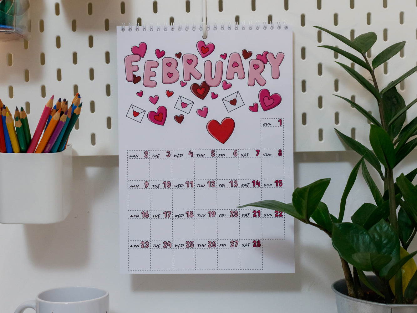 2026 Wall Calendar: February page with heart decorations on a pegboard wall with stationery items.
