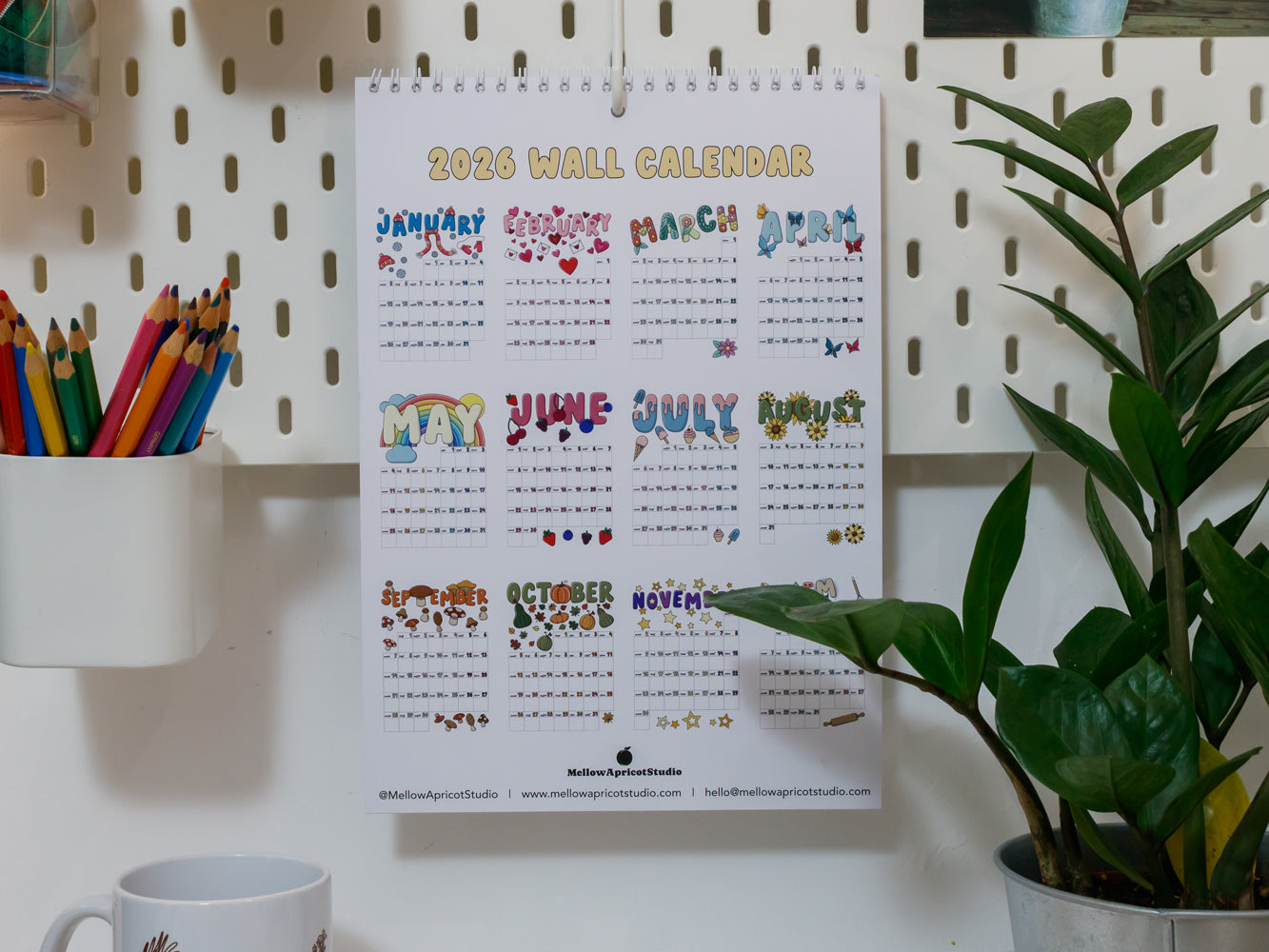 2026 wall calendar with colourful designs on a white pegboard with stationery items.