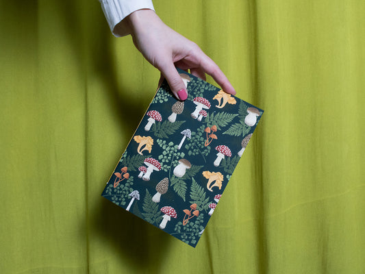 Hand holding a sketchbook with a colourful mushroom pattern against a green background