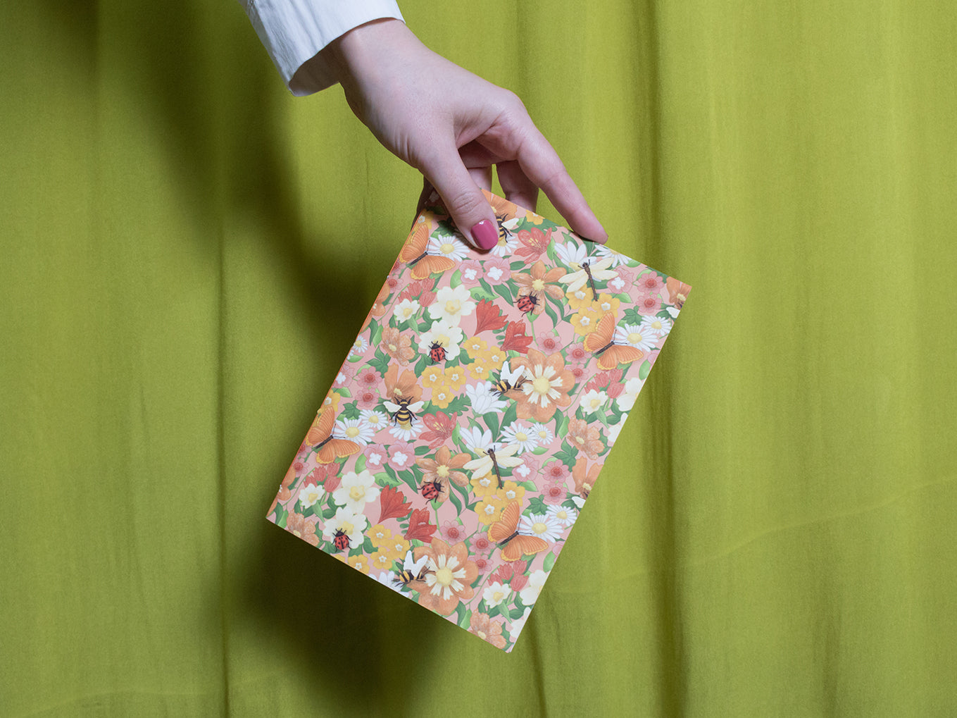 Hand holding a floral sketchbook against a green background