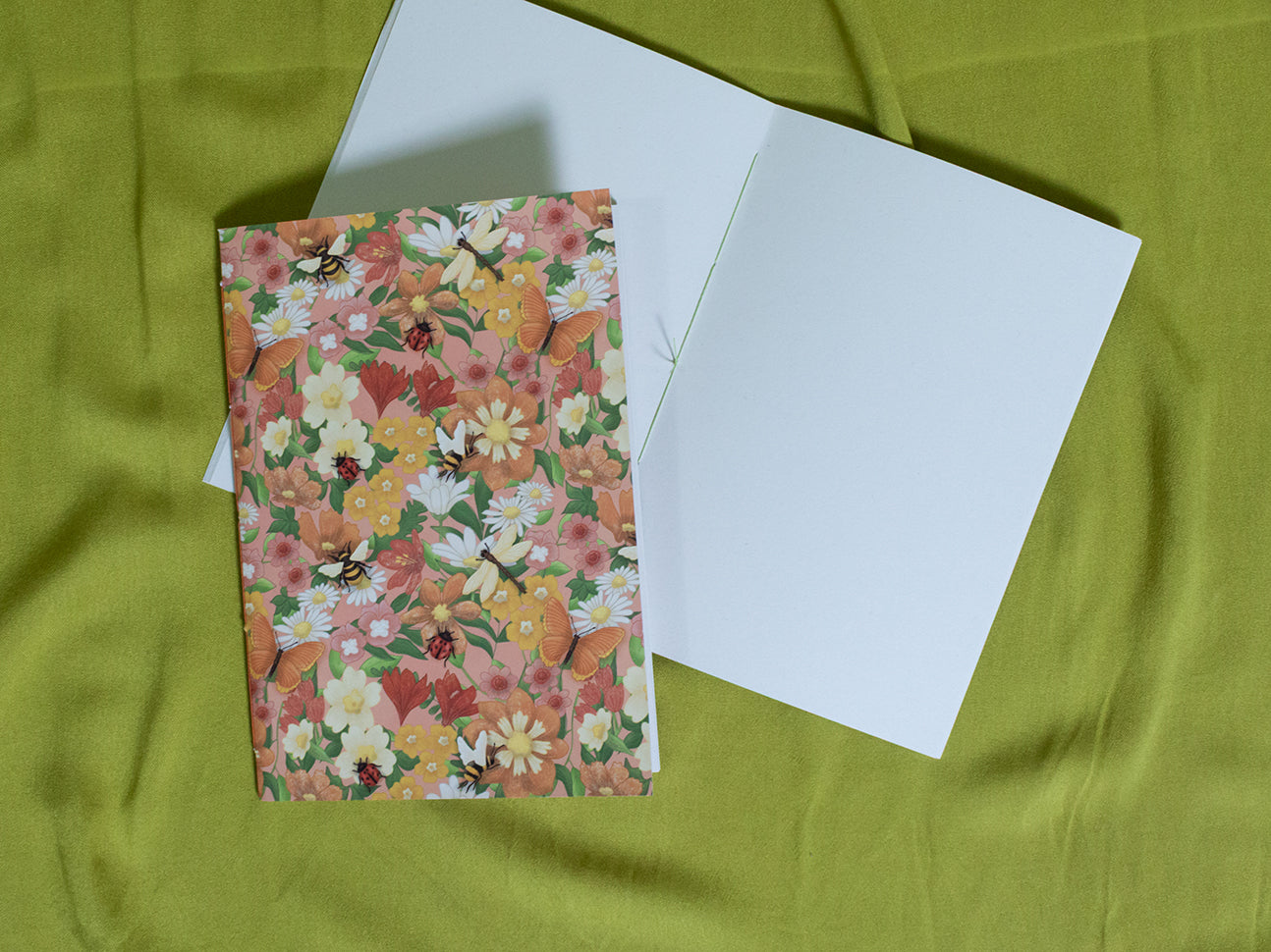 Floral sketchbook and white paper on a green fabric background