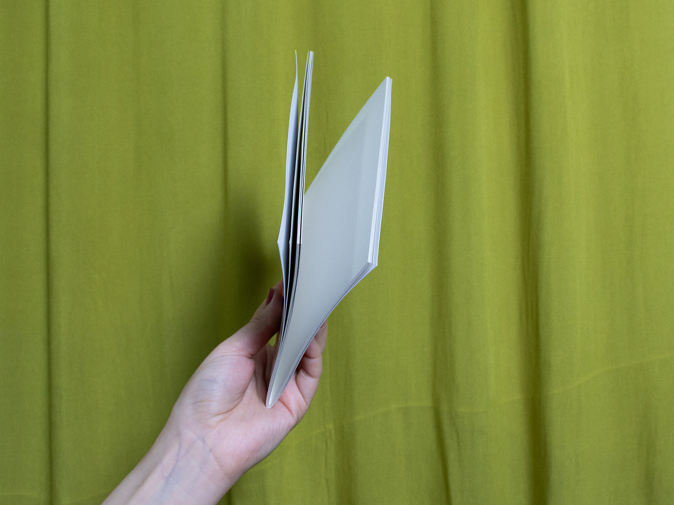 Hand holding a sketchbook against a green curtain background