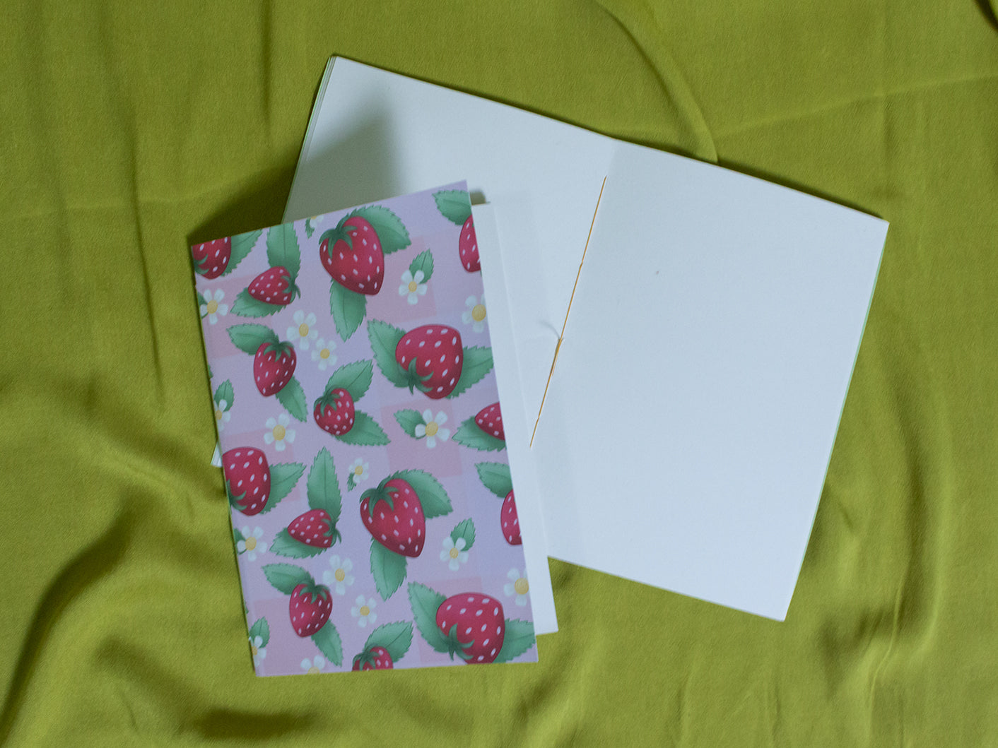 Sketchbook with strawberry pattern on a green fabric background