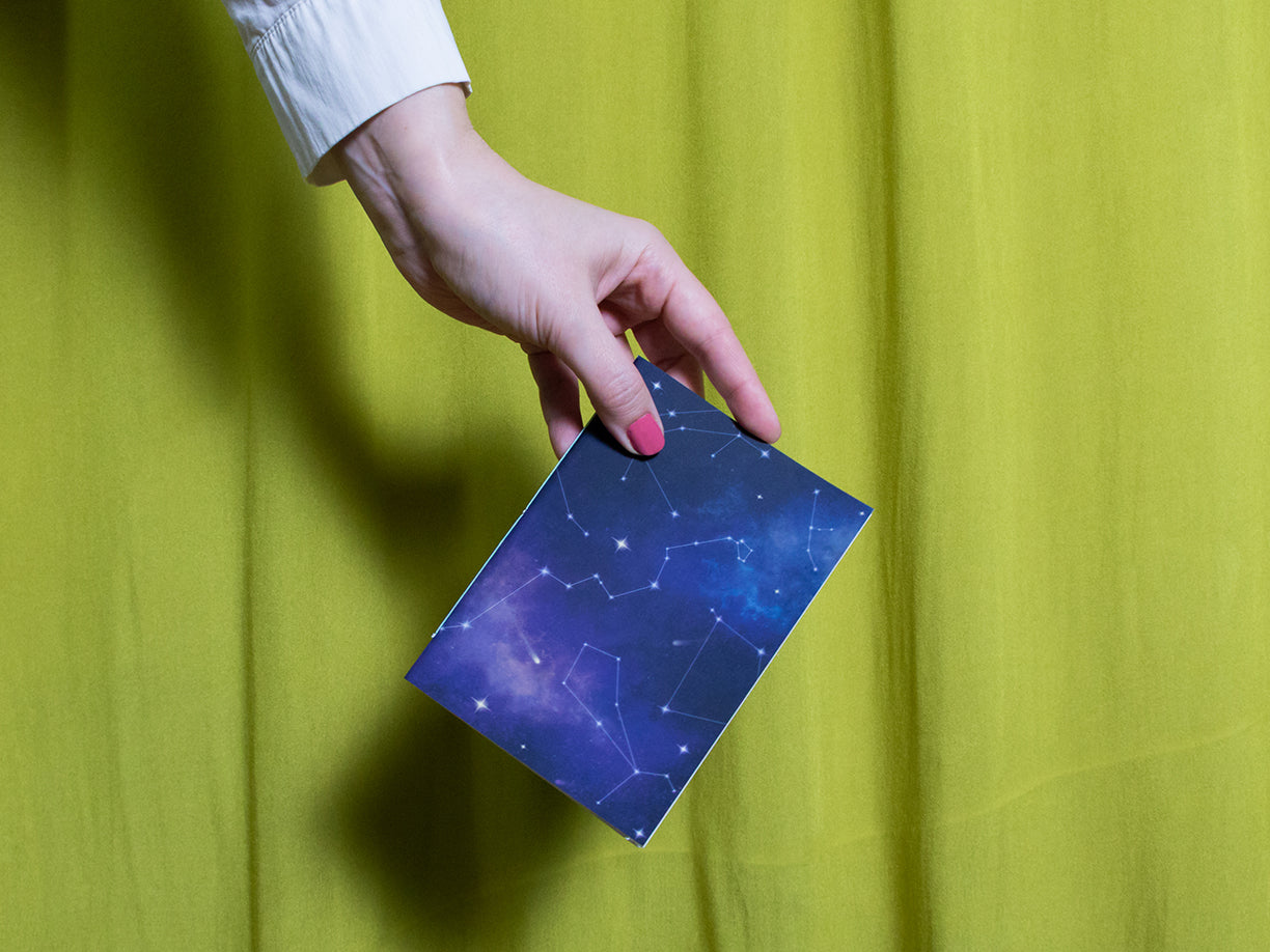 Hand holding a blue sketchbook with star patterns against a green curtain background