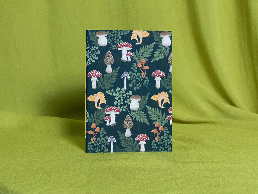 Small sketchbook with a forest-themed design featuring mushrooms and foliage on a green fabric background