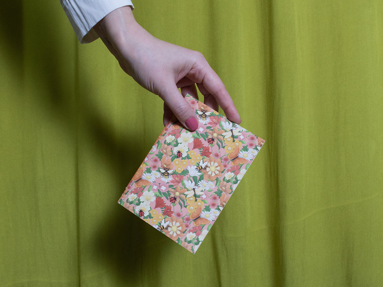 Hand holding a small floral sketchbook against a green curtain