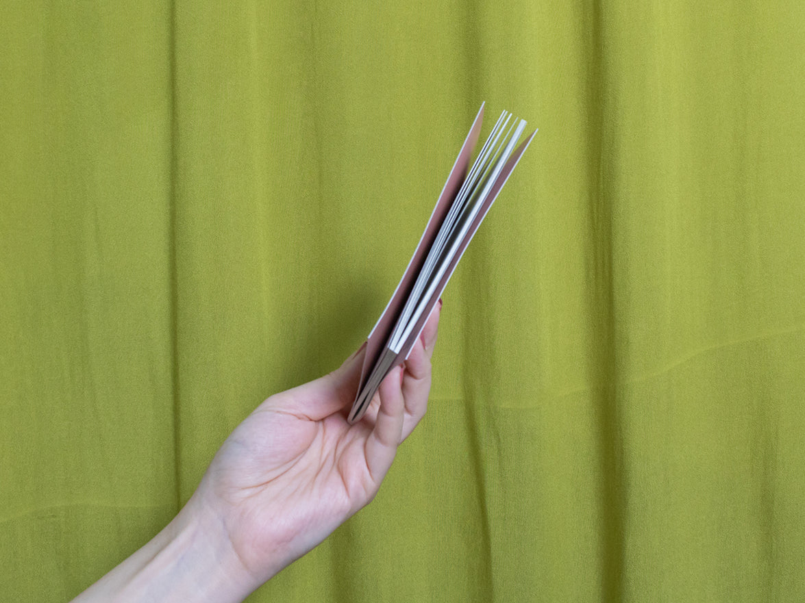 Hand holding a small sketchbook against a green curtain background