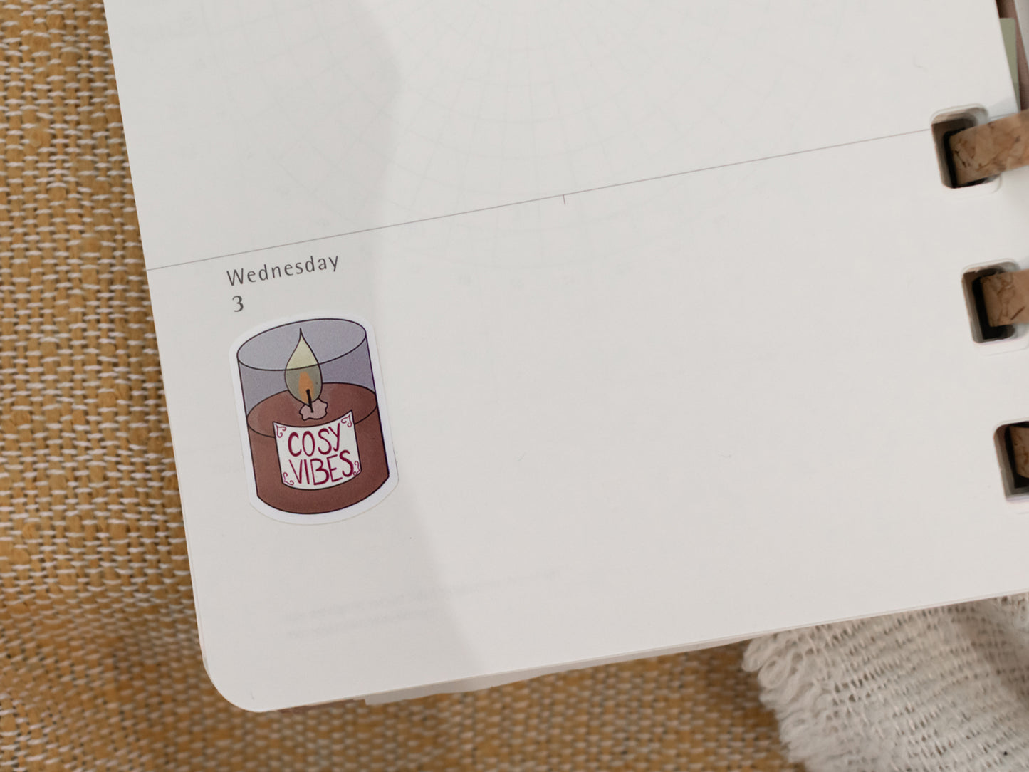 Calendar page with a sticker of a candle labeled 'Cosy Vibes' on a textured surface.