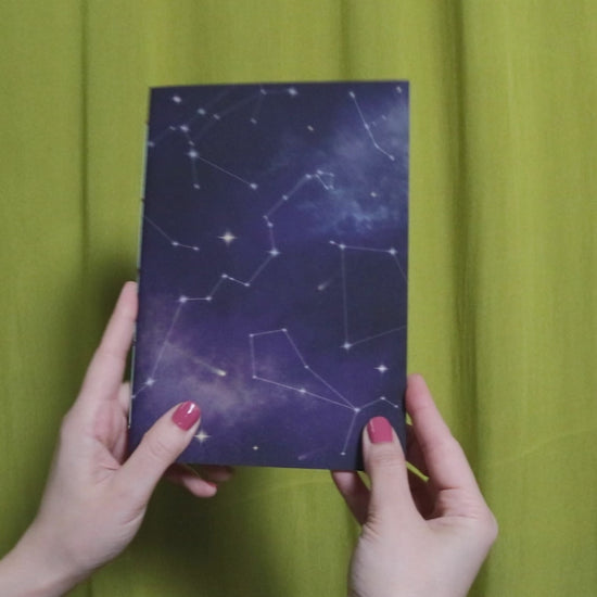 Video of two hands holding and flipping through a sketchbook with cosmic pattern against a green curtain background