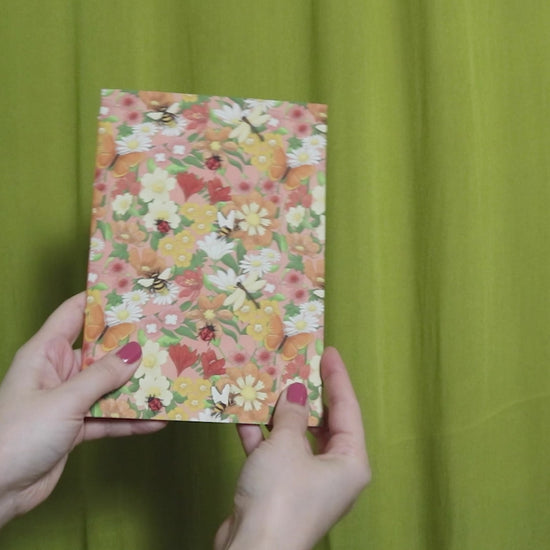 Video of two hands holding and flipping through a sketchbook with floral pattern against a green curtain background
