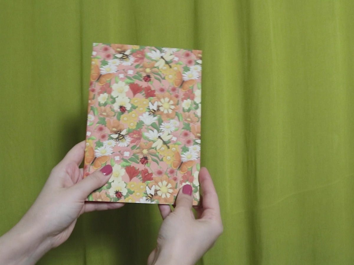 Video of two hands holding and flipping through a sketchbook with floral pattern against a green curtain background