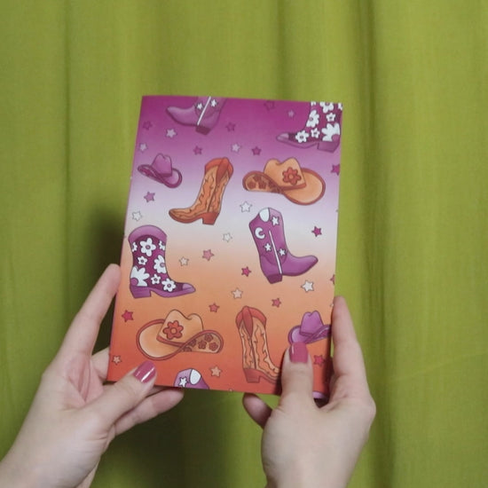 Video of two hands holding and flipping through a sketchbook with howdy pattern against a green curtain background
