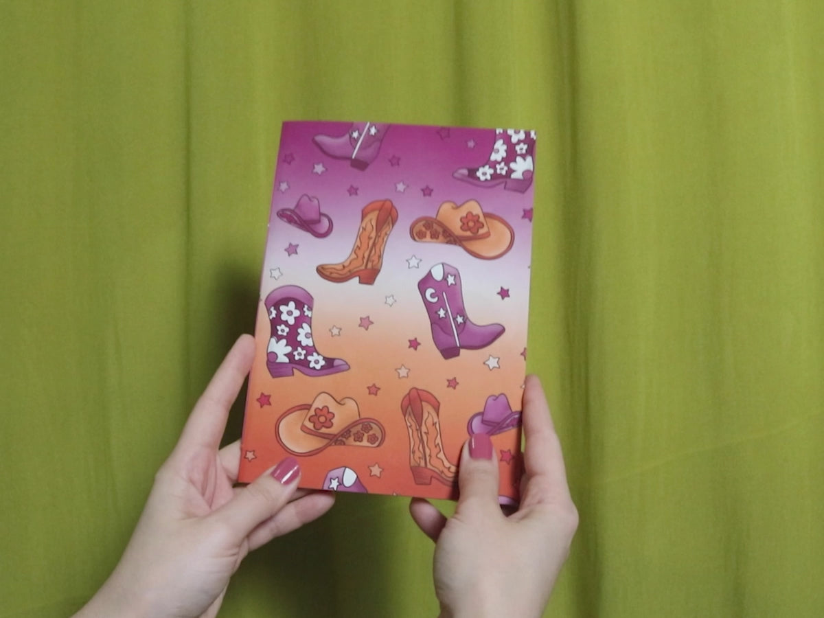 Video of two hands holding and flipping through a sketchbook with howdy pattern against a green curtain background