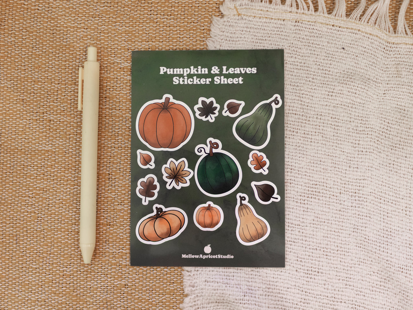 Sticker sheet with pumpkins and leaves on a textured surface next to a pen for scale