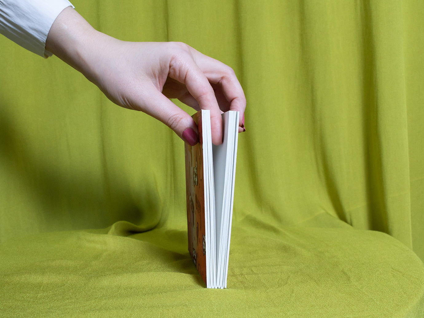 Hand holding a square sketchbook with cowboy pattern against a green fabric background
