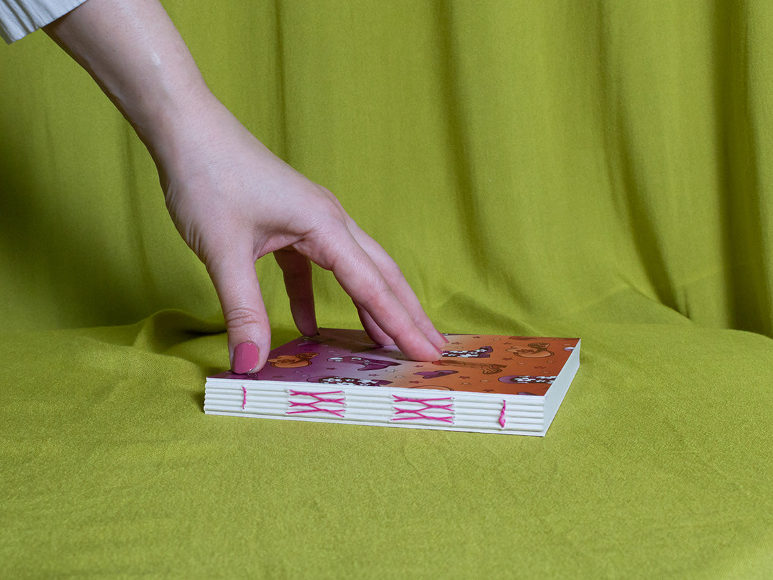 Hand reaching for a square sketchbook with cowboy pattern on a green fabric background