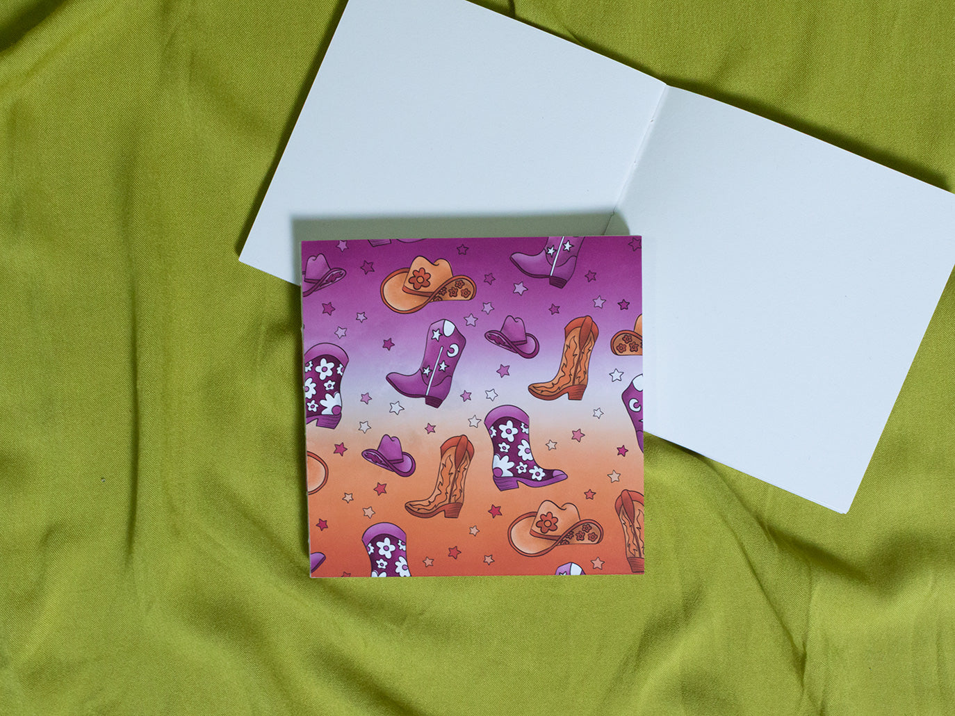 Colourful square sketchbook with cowboy boots and hats on a green fabric background