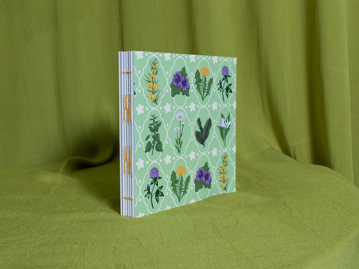 Open spine sketchbook with floral design on a green fabric background