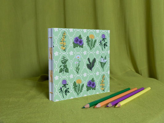 Square sketchbook with floral design on a green background with coloured pencils.