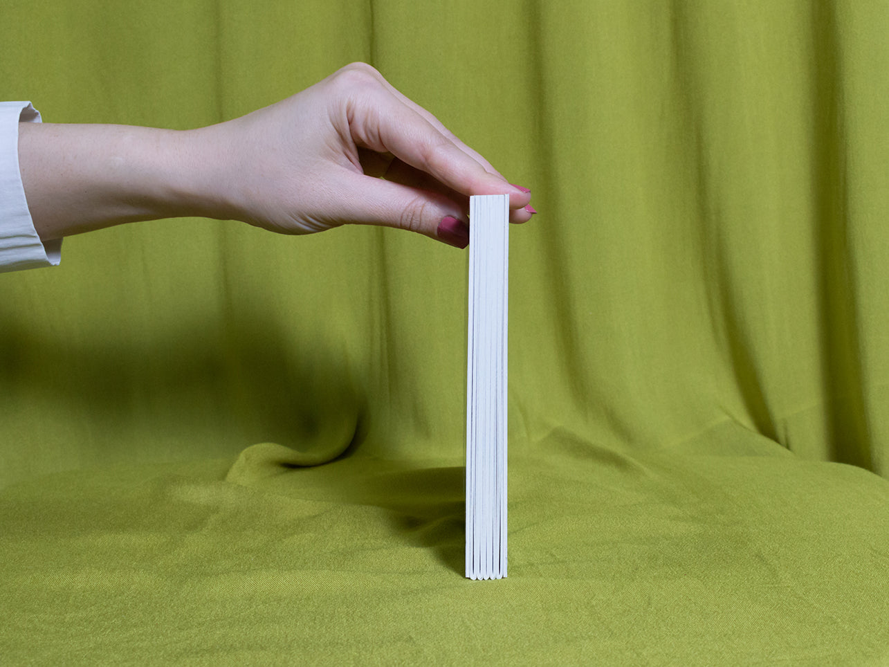 Hand holding a sketchbook sideways against a green fabric background