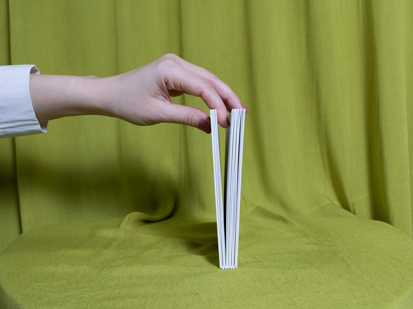 Hand holding a sketchbook against a green fabric background