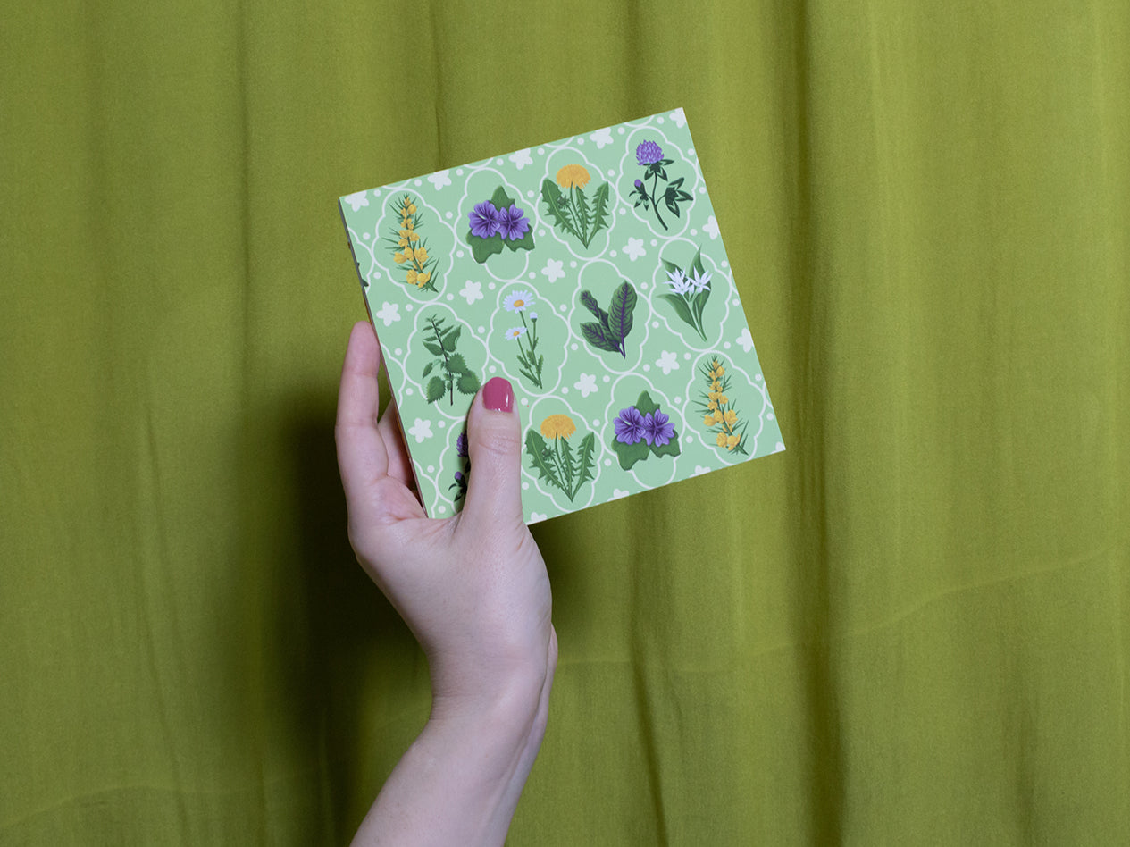 Hand holding a green sketchbook with floral patterns against a green background