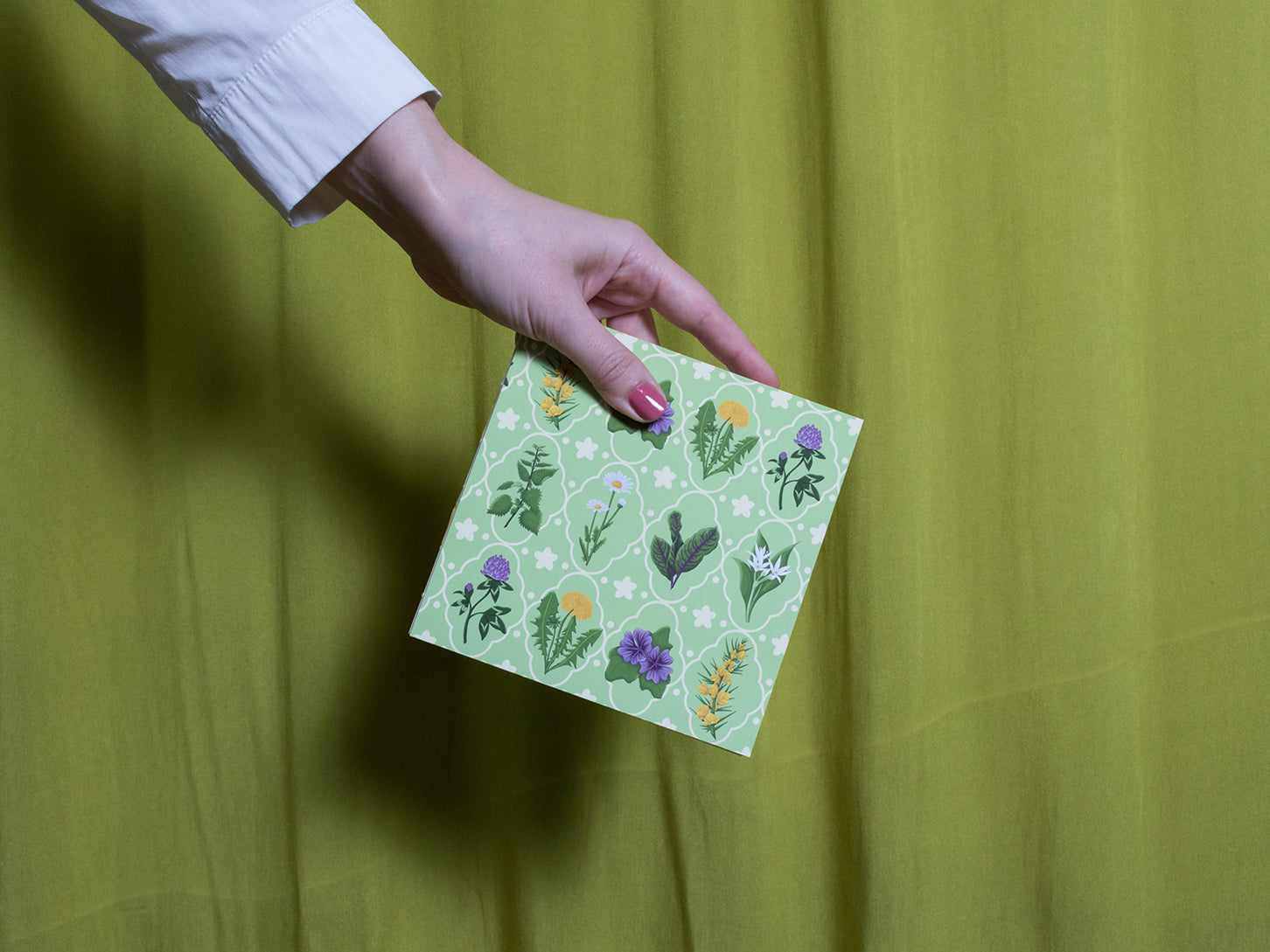 Hand holding a green sketchbook with floral patterns against a green background