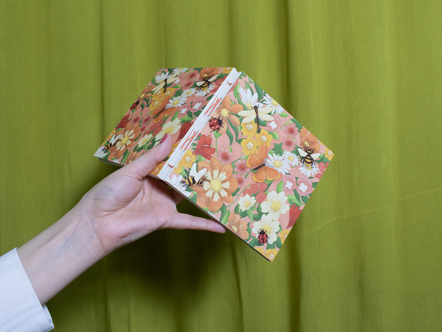 Hand holding a floral-patterned sketchbook against a green background